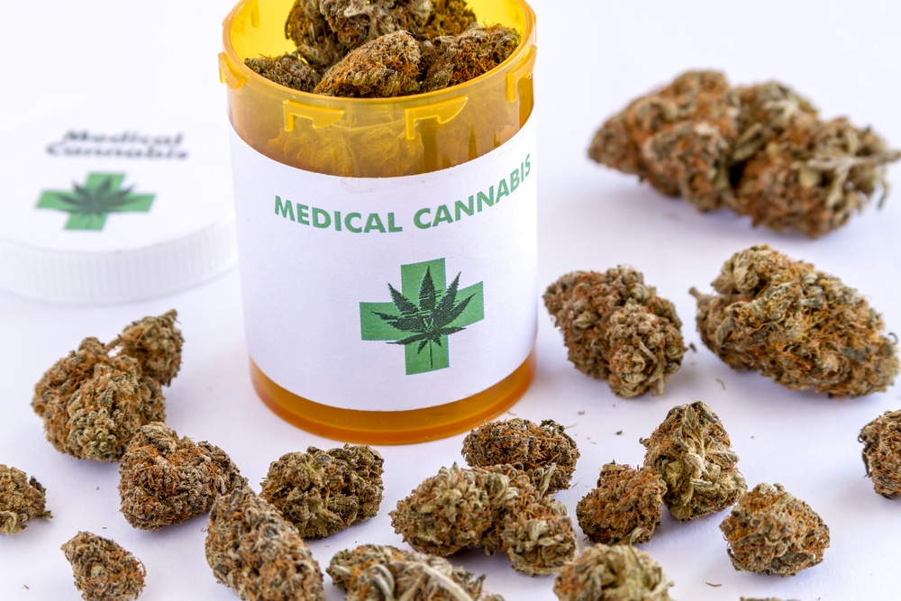 Medical marijuana buds sitting on white table top next to medical cannabis prescription bottle with lid
